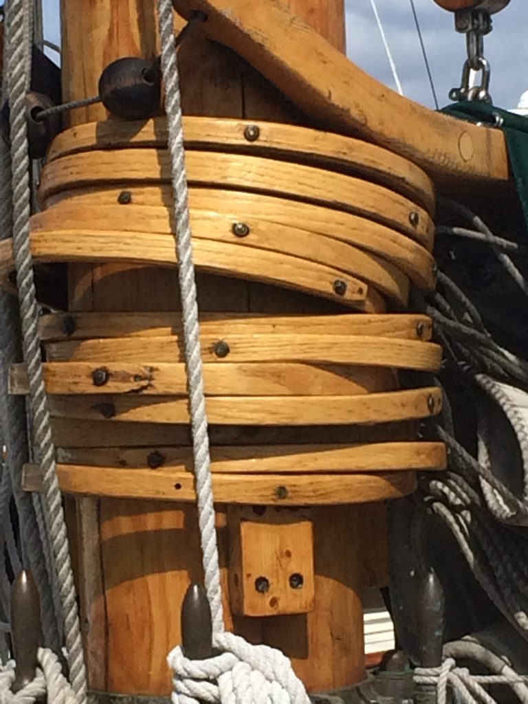 Wooden mast with coiled rigging and rope details, showcasing craftsmanship of the Liberty, a classic Friendship sloop in San Diego Bay.